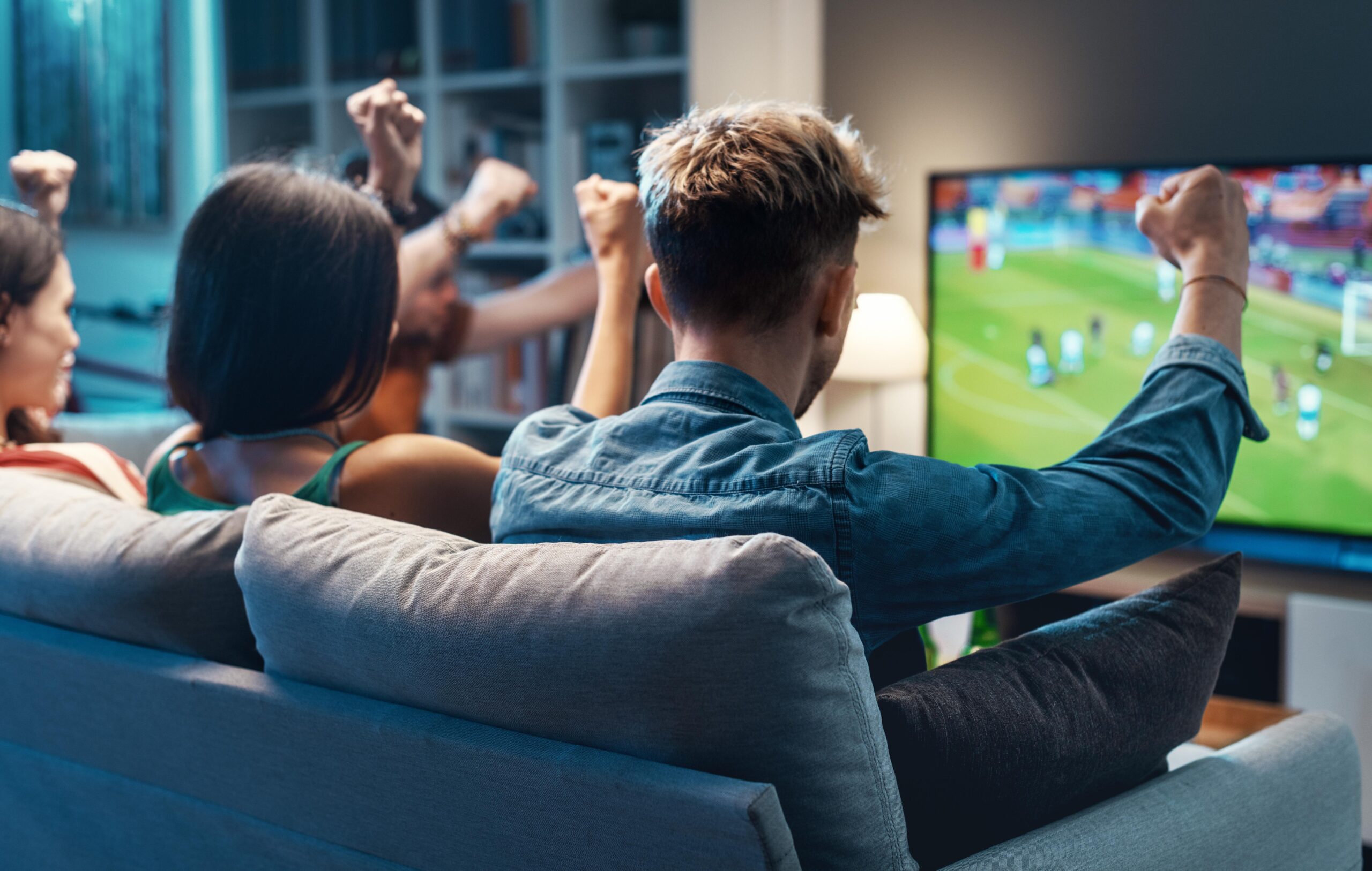 Group of young friends watching a football match on TV together and cheering for their team